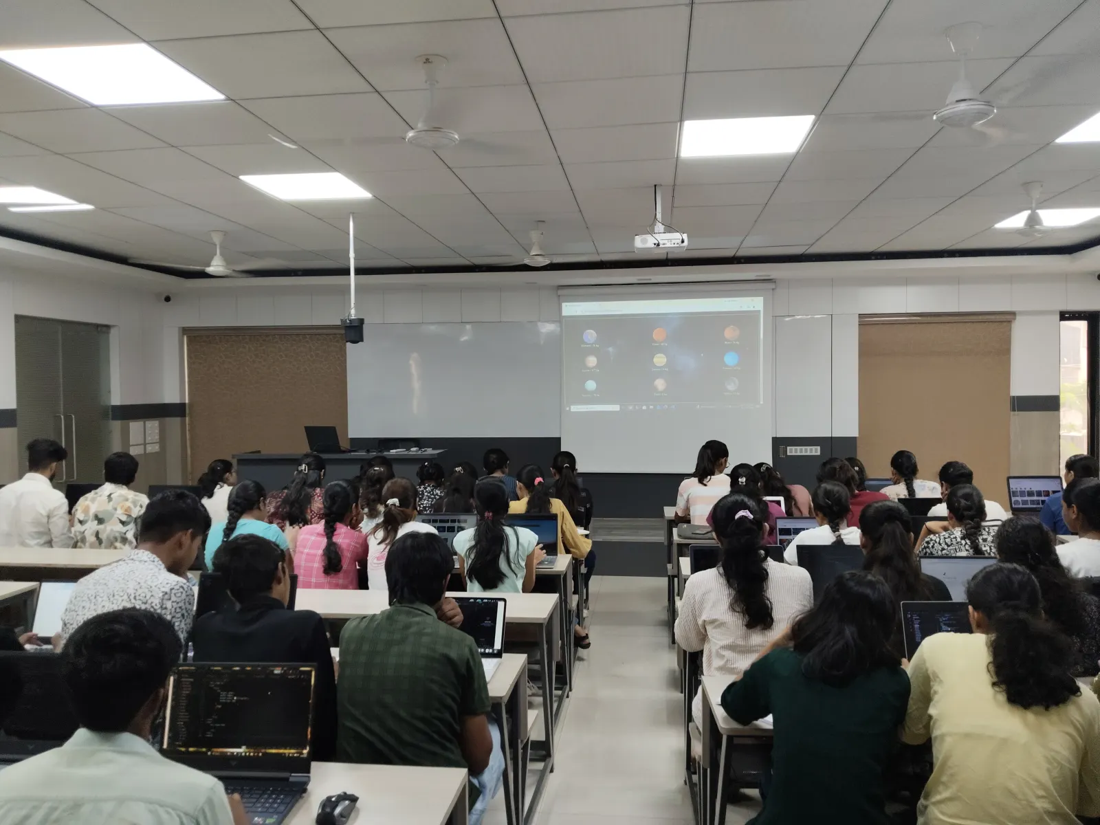 Students coding on laptops facing the projector at Info Planet, Jalgaon
